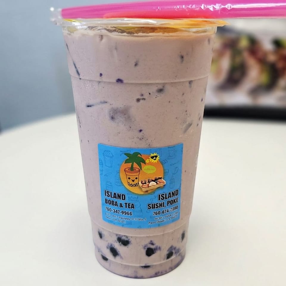A clear cup of creamy brown bubble tea with tapioca pearls, pink straw, and Island Boba & Tea label on a table.