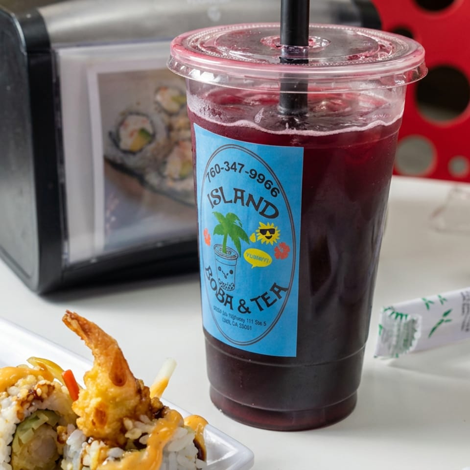 Sushi rolls with shrimp and sauce sit beside an iced drink labeled Island Boba & Tea on a restaurant table.